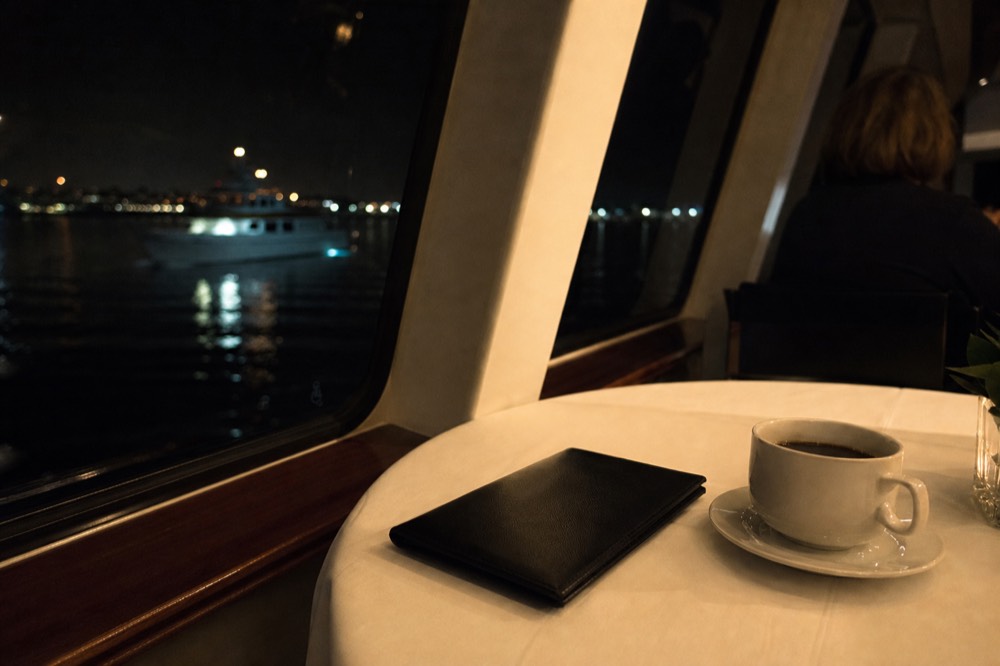 Bill folder and coffee on a white tablecloth beside a ship window at night on a San Diego dinner cruise
