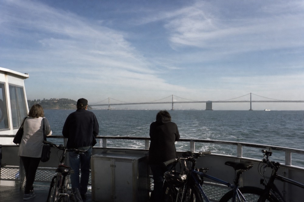 Passengers and bicycles on the open deck of the Coronado ferry crossing San Diego Bay with the bridge ahead