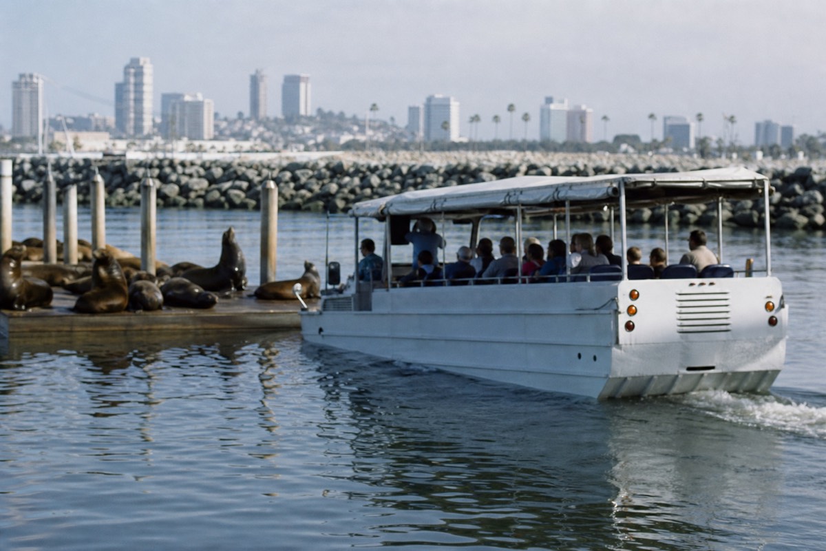 Passengers aboard an amphibious SEAL Tour vehicle cruising San Diego Bay past Navy ships