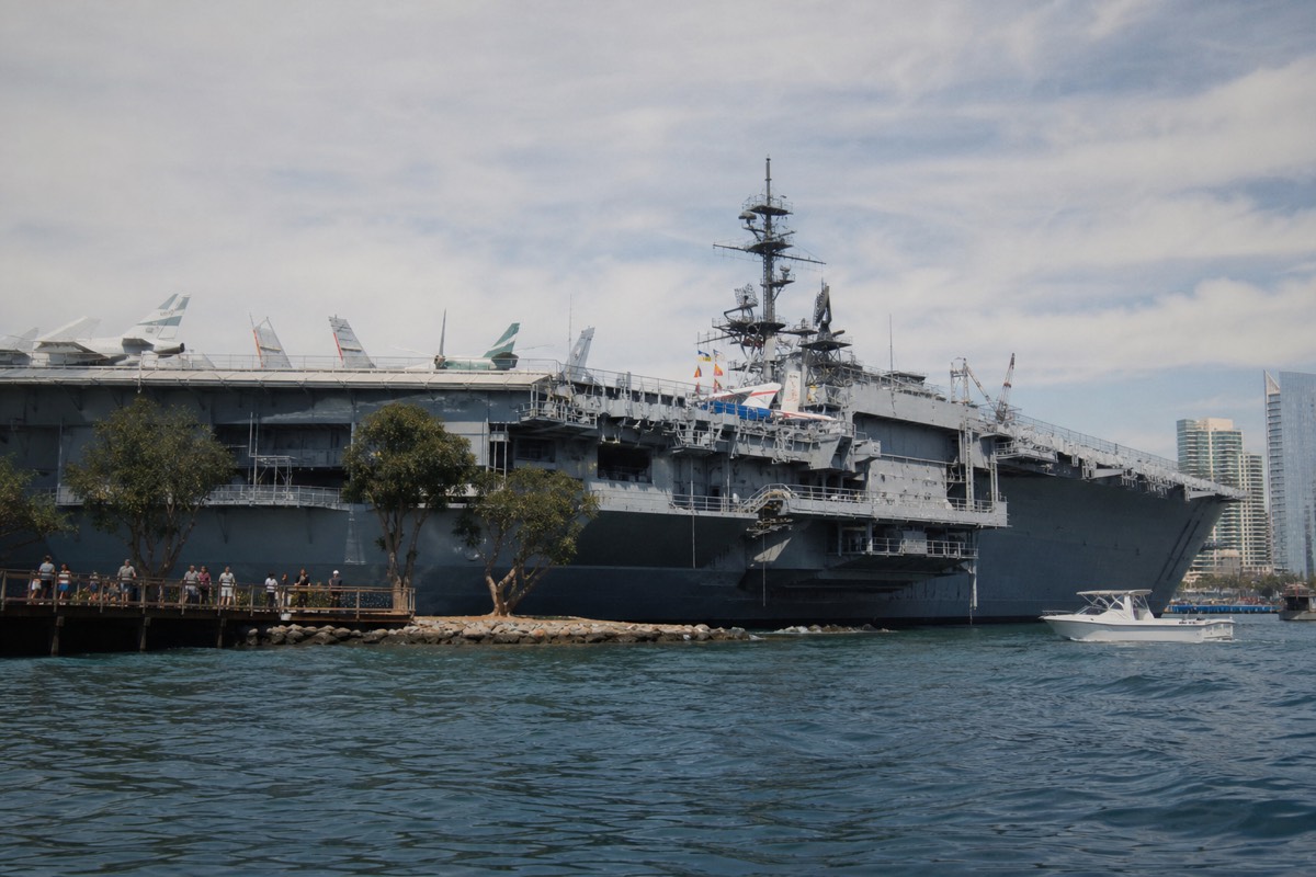 Large grey aircraft carrier berthed on the downtown San Diego waterfront seen from a boat on the bay