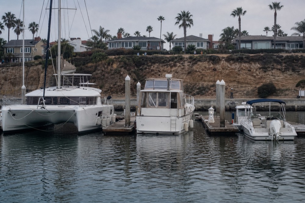 Three different San Diego whale watching boats at their docks in one marina basin, a sailing catamaran, a cabin boat and an open boat