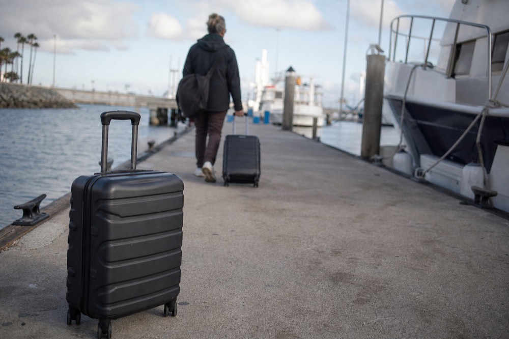 Passengers wheeling suitcases along the San Diego Embarcadero promenade with cruise ship funnels ahead