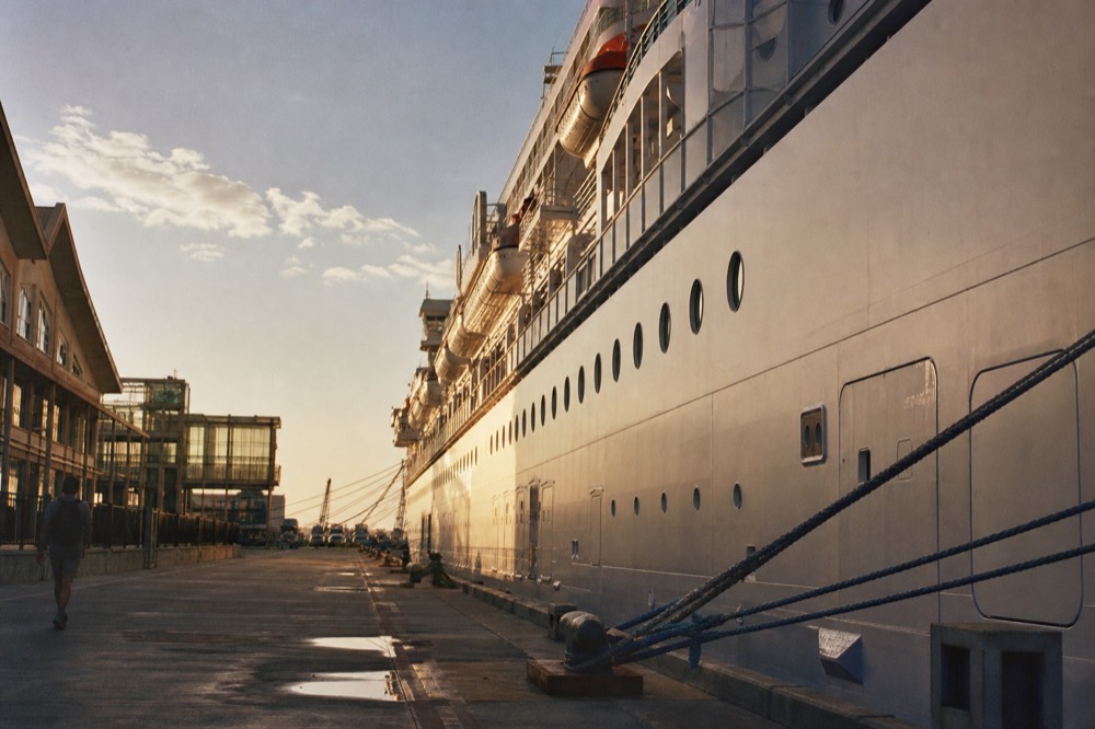 A large white cruise ship at the San Diego Embarcadero terminal at golden hour, long shadows and warm low light