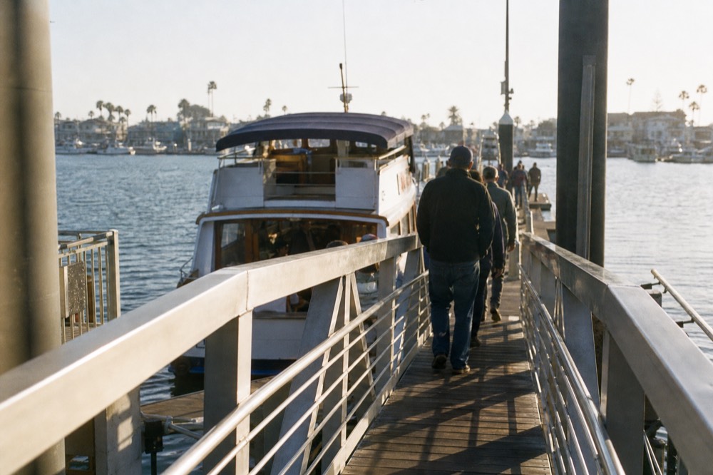 Gangway leading down to a floating dock where a San Diego cruise boat waits in long morning shadows
