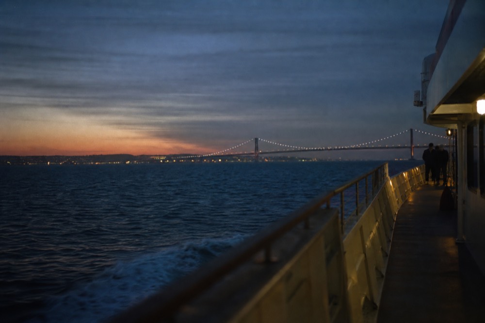 Stern rail of a San Diego dinner cruise at dusk with a lit bridge across dark bay water