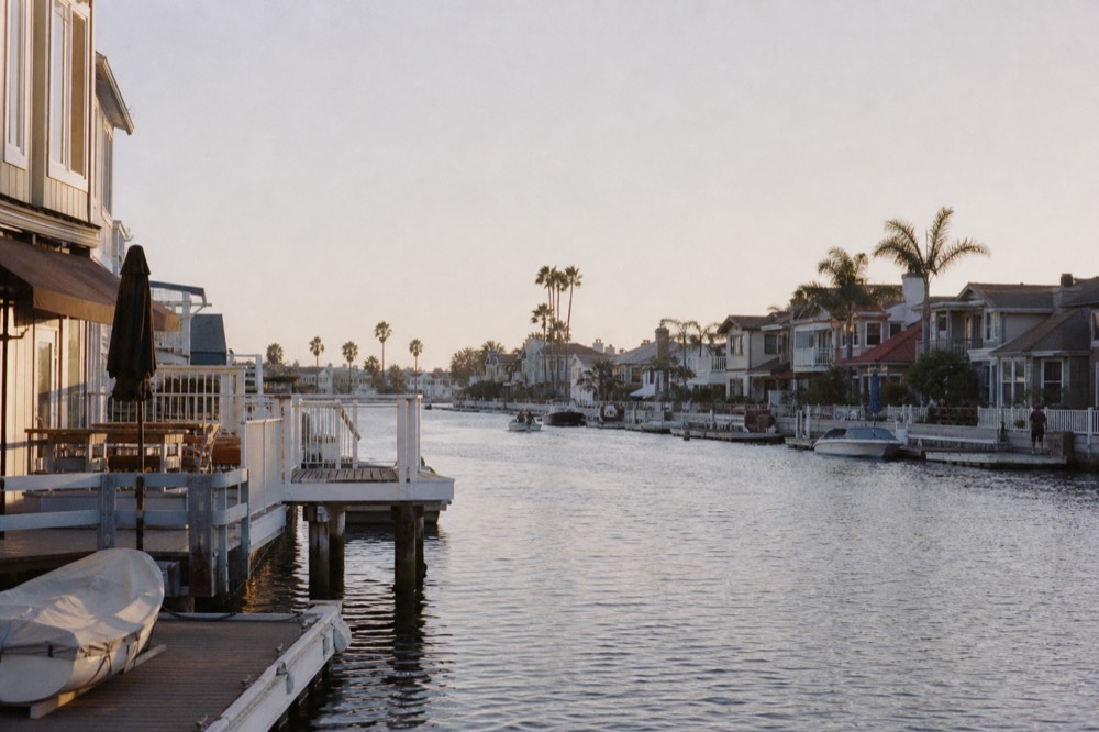 Waterfront homes with private docks lining a calm Coronado Cays canal at golden hour, the water flat enough to mirror them