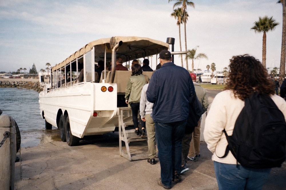 Amphibious San Diego SEAL Tour vehicle parked at a waterfront plaza with passengers boarding under the palms
