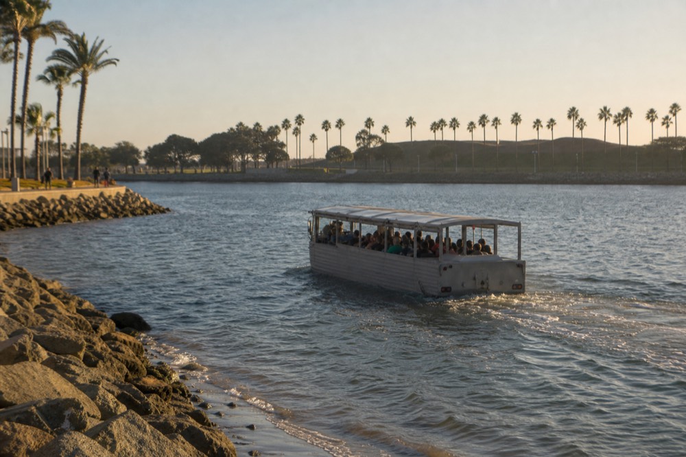 A boxy amphibious sightseeing vehicle around San Diego's palm-lined waterfront at golden hour, long shadows and warm low light