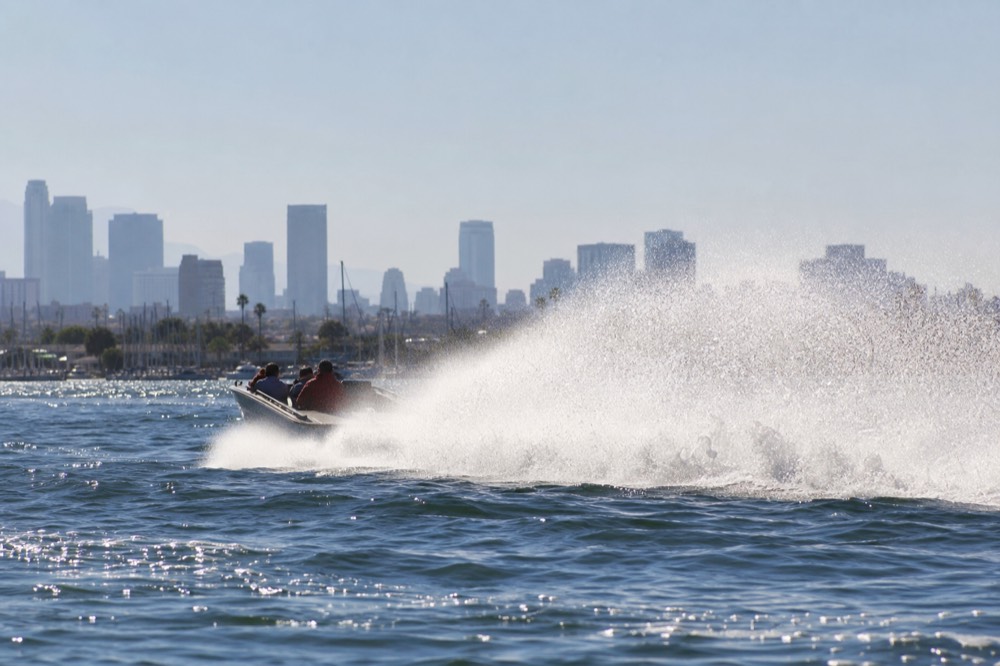 Jet boat throwing a rooster tail of spray at speed on San Diego Bay with the city skyline far behind