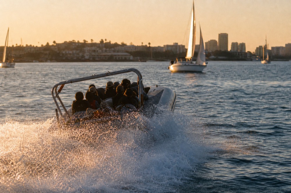 A fast open jet boat throwing spray on San Diego Bay at golden hour, long shadows and warm low light