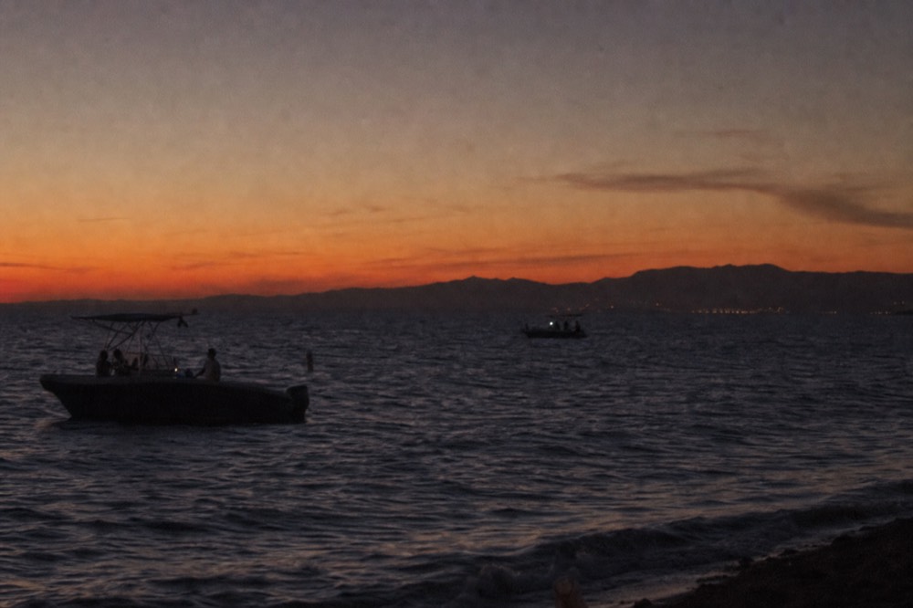 Deep orange afterglow over dark water about twenty minutes after a San Diego sunset cruise passes the point, boats in silhouette against the colour