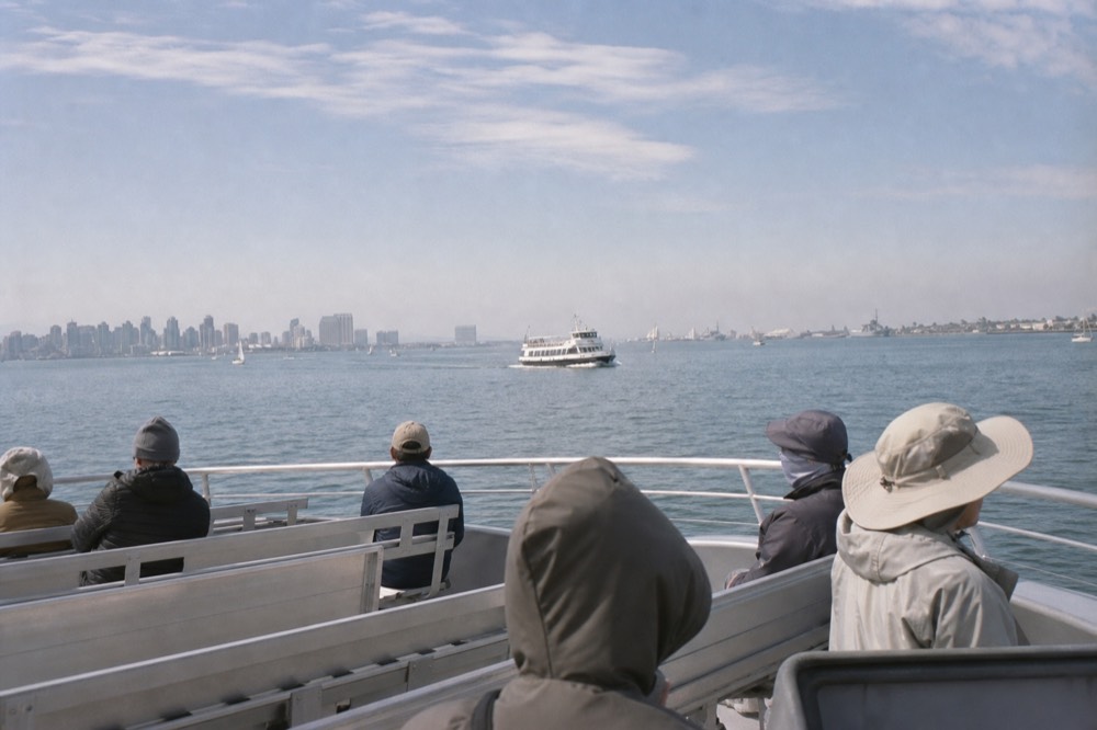 Passengers dressed in layers for wind and sun on a San Diego boat deck, late-morning light