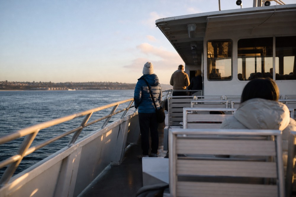 Passengers dressed in layers for wind and sun on a San Diego boat deck at golden hour, long shadows and warm low light