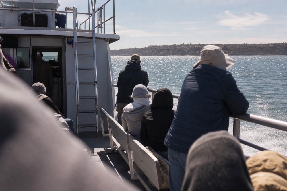 Passengers dressed in layers for wind and sun on a San Diego boat deck, a railing or shoulder softly out of focus in the foreground